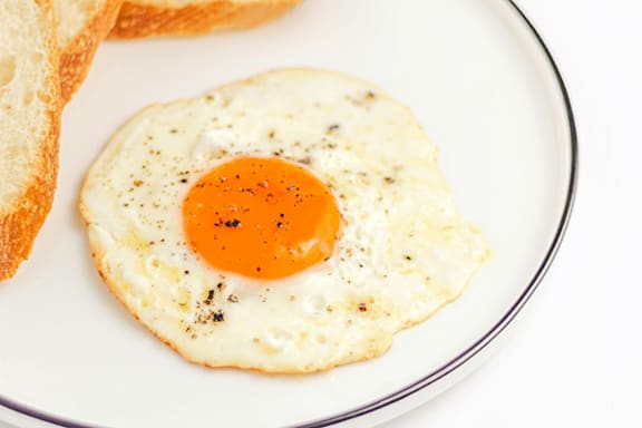A fried egg with a runny yolk on a white plate.