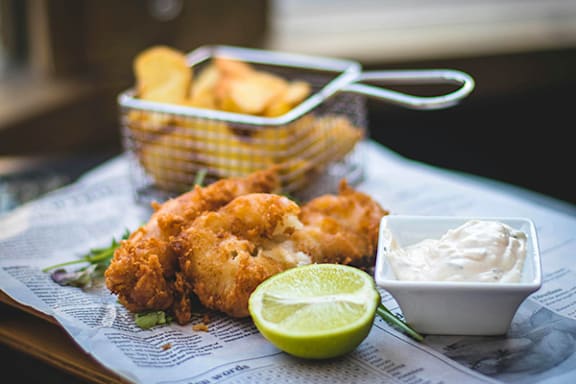 a basket of fried shrimp next to a container of chips and a lemon wedge