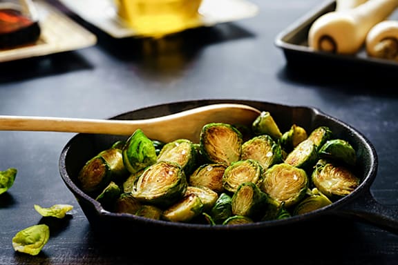 A pan of cooked Brussels sprouts with a wooden spoon in it.