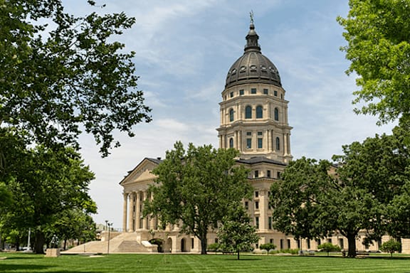 A large, stately building with a dome and columns stands in a grassy area with trees.