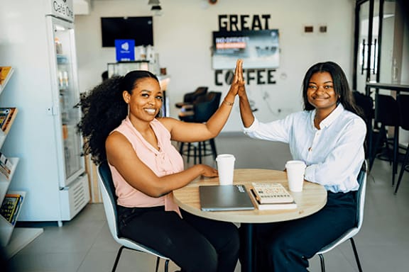 Two women high-five each other at a table in a cafe.
