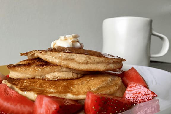 A stack of pancakes topped with whipped cream and served with strawberries.