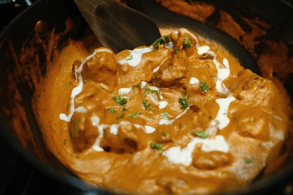 A creamy, orange-colored curry with chunks of meat and a drizzle of cream on top.