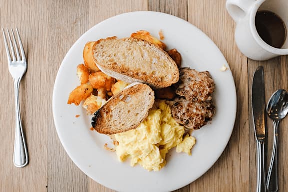A breakfast plate with scrambled eggs, toast, and sausage.