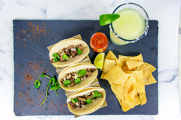 A plate of tacos and chips with a drink on the side.