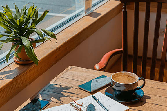 A cup of coffee and a plant on a wooden table by a window.