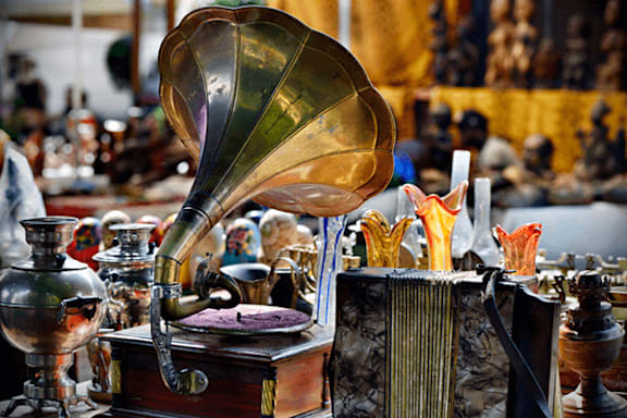 A vintage gramophone with a shiny brass horn sits on a table surrounded by other antique items.