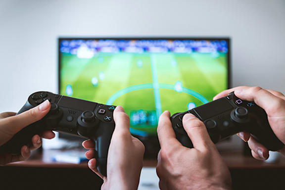 Two hands holding black game controllers in front of a television screen displaying a soccer game.