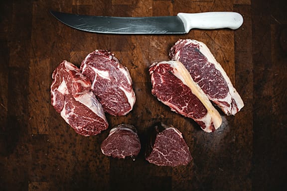 A knife is placed on a wooden cutting board with a few slices of meat.