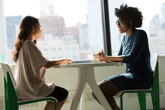 Two women sitting at a table in a bright room.