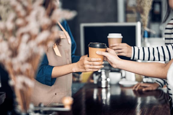 A person in a striped shirt is handing a coffee cup to another person in a blue shirt.