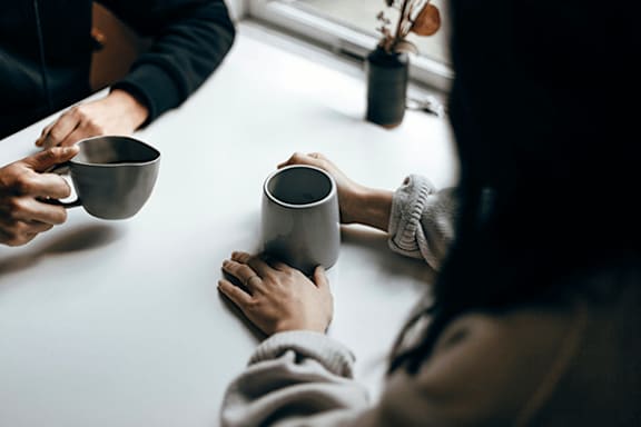 Two people holding mugs in front of a window.