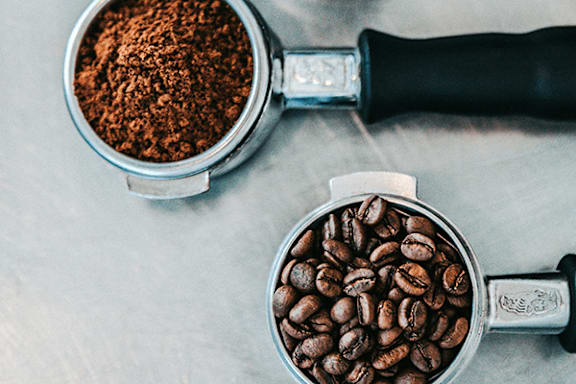 A coffee grinder and a cup of ground coffee on a grey surface.