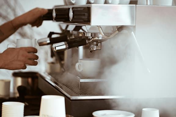 A barista is making a cup of coffee using a professional espresso machine.