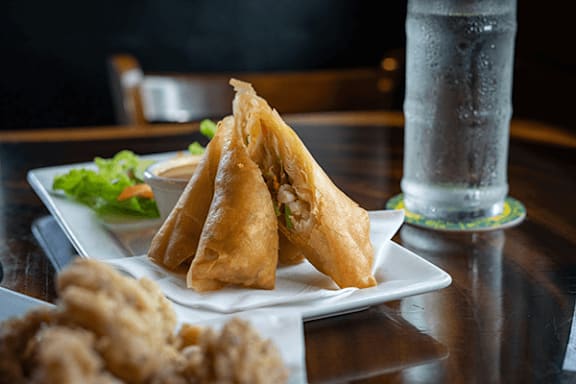 A plate of fried wontons and fried chicken pieces with a glass of water in the background.