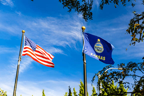 Two flags, one of the United States and one of Kansas, are flying side by side.