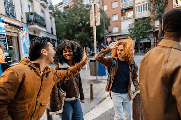 A man in a brown jacket is pointing at a woman with curly hair who is wearing a blue top and white pants.