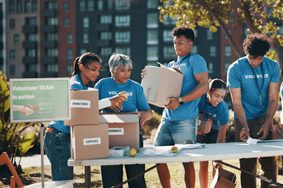 A group of people in blue shirts are volunteering and sorting through boxes of donations.
