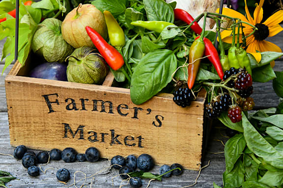 A wooden box labeled "Farmer's Market" is filled with fresh produce.