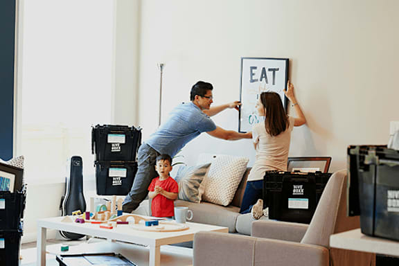 A man and woman are holding up a sign that says "EAT" in a living room with a child sitting on the couch.