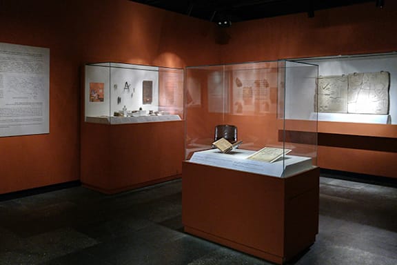 A display case with artifacts inside and a wall of documents behind it.