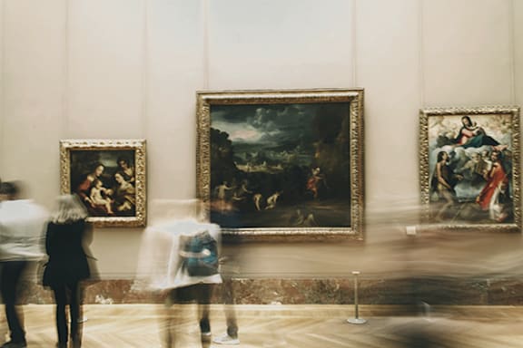 Three people are walking past paintings in a museum.