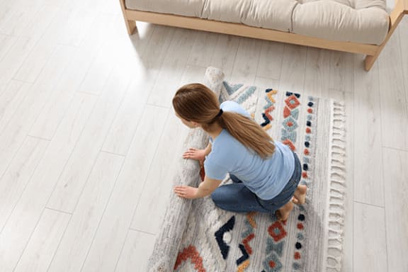 A woman is sitting on a rug in a room with a wooden floor and a sofa in the background.