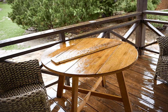 A wooden table with a chair and a pine tree in the background.