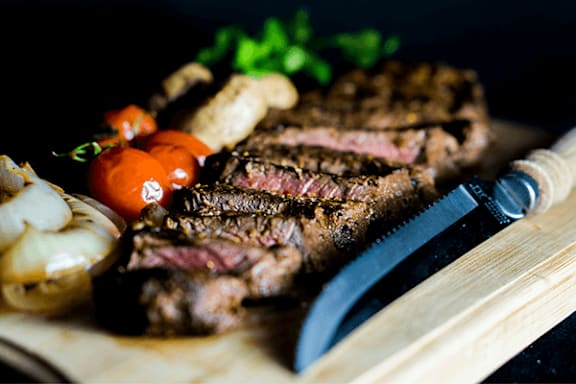 A steak is sliced and served with onions and tomatoes.