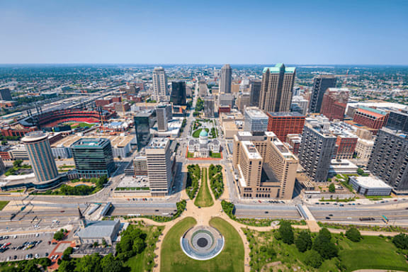 A cityscape with a mix of modern and older buildings, a large open space with a circular design, and a clear sky.