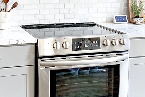 A modern stainless steel oven with a glass door is installed in a kitchen with a white tile backsplash.