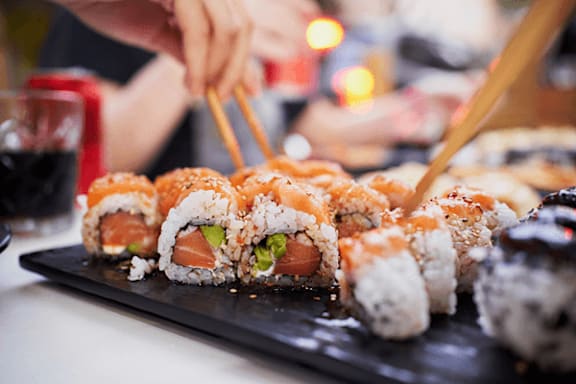 A person is holding chopsticks over a plate of sushi.