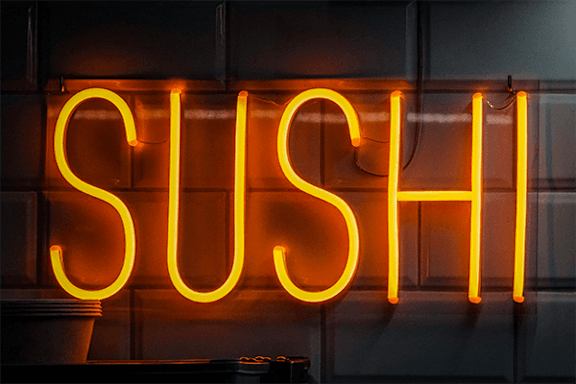 A neon sign that says "SUSHI" in bright orange.
