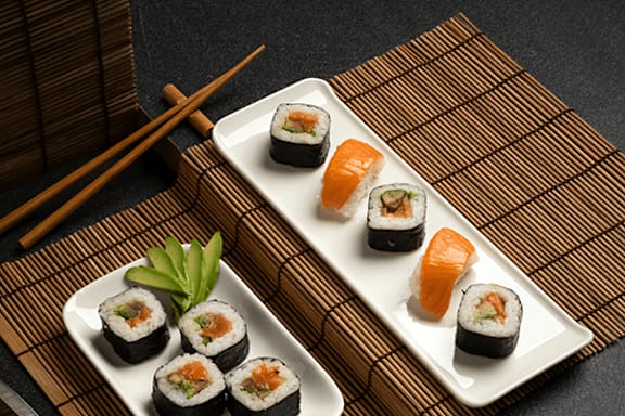 Two plates of sushi with chopsticks on a bamboo mat.