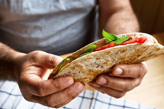 A person is holding a wrap with vegetables inside.