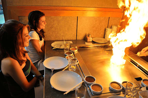Two women are standing in front of a counter with a fire on it.