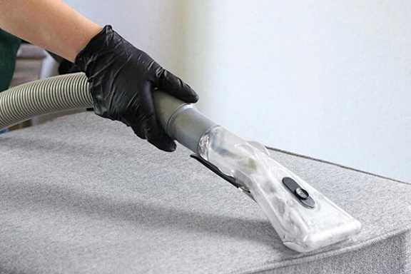 A person wearing black gloves vacuums a grey carpet.