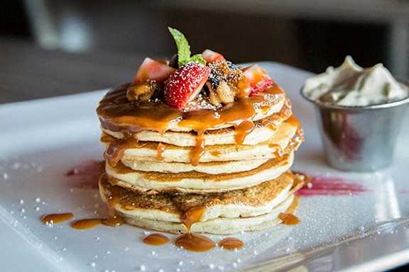 A stack of pancakes topped with strawberries, chocolate, and whipped cream.