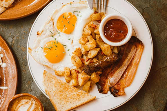 a plate of breakfast food with eggs bacon and toast and a cup of ketchup