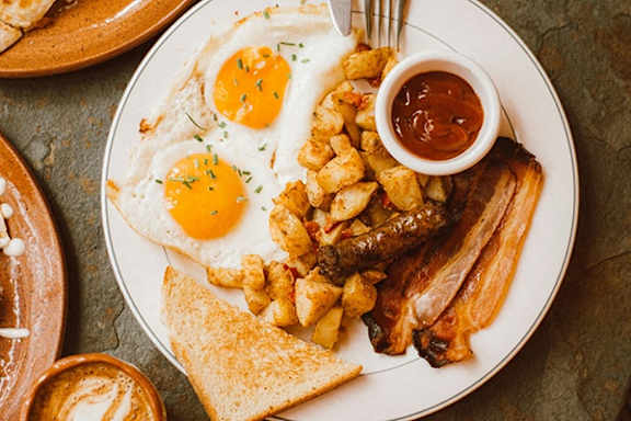 A breakfast plate with eggs, bacon, sausages, hash browns, and toast.