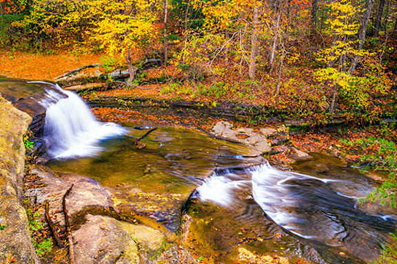 A small waterfall flows over rocks in a forest.