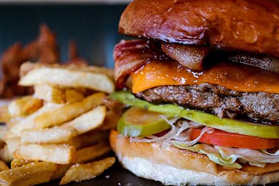 A close up of a burger with bacon, cheese, tomato, and lettuce.