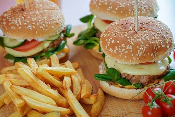 Three burgers with cheese, tomato, and lettuce on sesame seed buns are served with a side of fries.