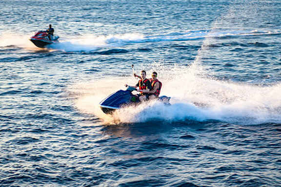 Two jet skis with people riding them are speeding through the water.