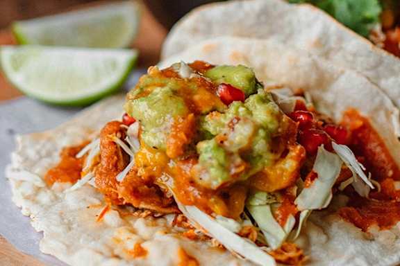 A taco with cheese, guacamole, and tomatoes on a white tortilla.
