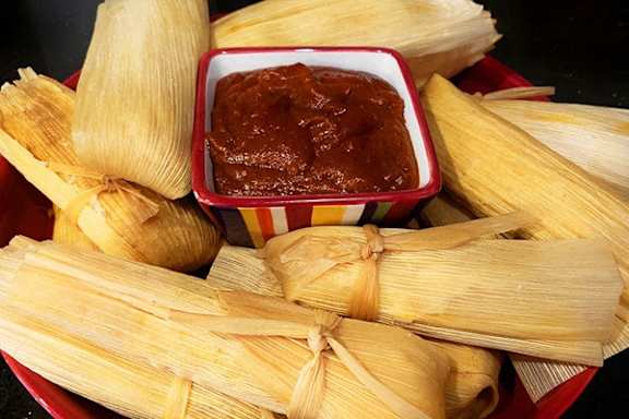 A red bowl filled with tamales and a bowl of salsa.