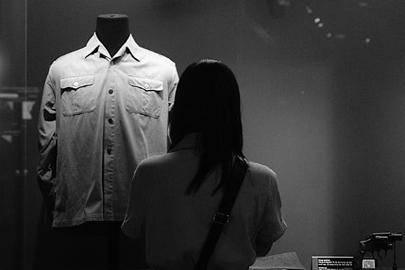 A woman is looking at clothes on a rack in a room with two potted plants.