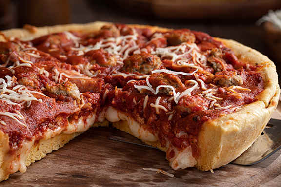 A pizza with a slice missing, topped with tomato sauce, cheese, and meat.