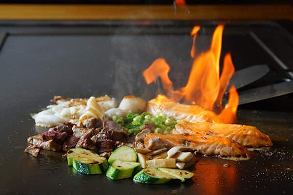 A variety of foods are being cooked on a grill with flames visible.