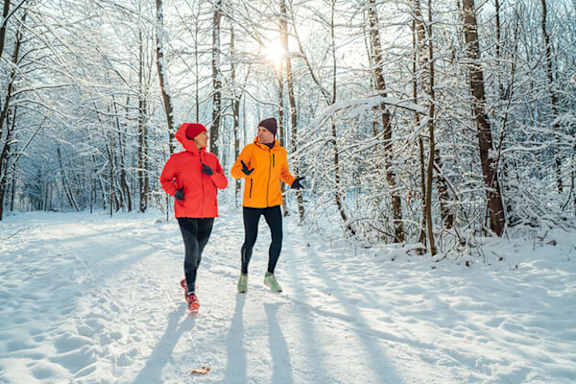 Two people jogging in a snowy forest.